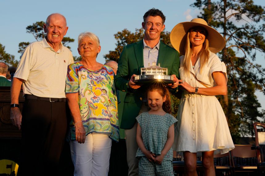 Rory McIlroy holds the Masters championship trophy while standing with his parents, Rosie and Gerry, his wife, Erica Stoll, and his daughter, Poppy, during the green jacket ceremony after the final round of the Masters Tournament at Augusta National Golf Club.